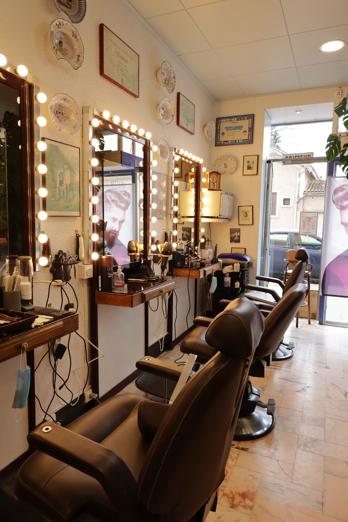 Les trois fauteuils du salon alignés devant les miroirs à ampoules, avec les assiettes décoratives et les diplômes accrochés au mur.
